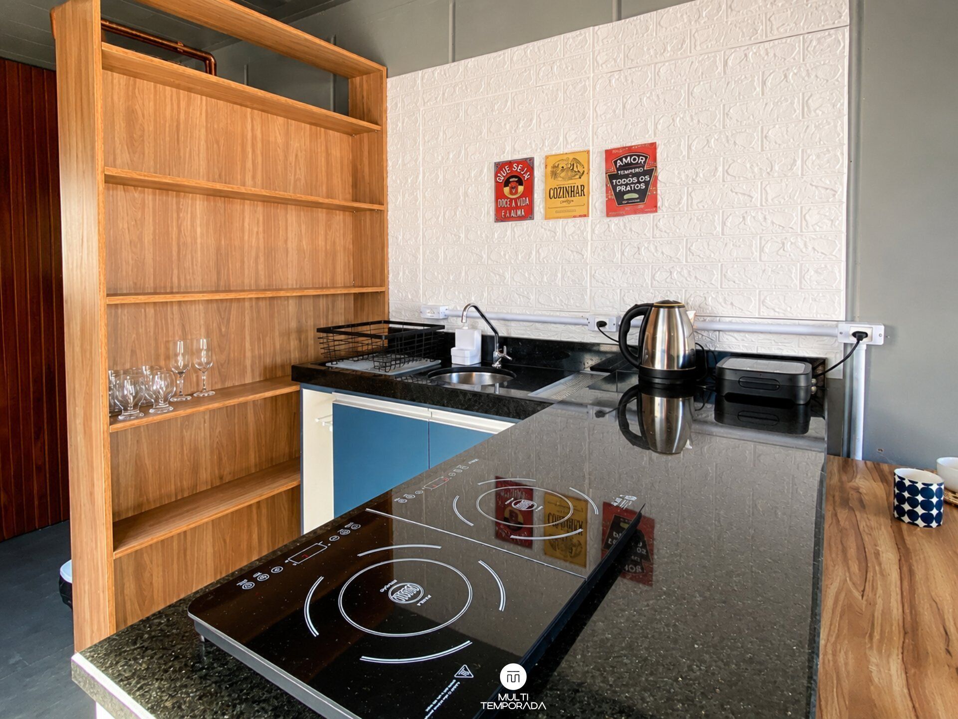 Una cucina moderna con piano cottura a induzione nero, mensole in legno e una macchina da caffè.