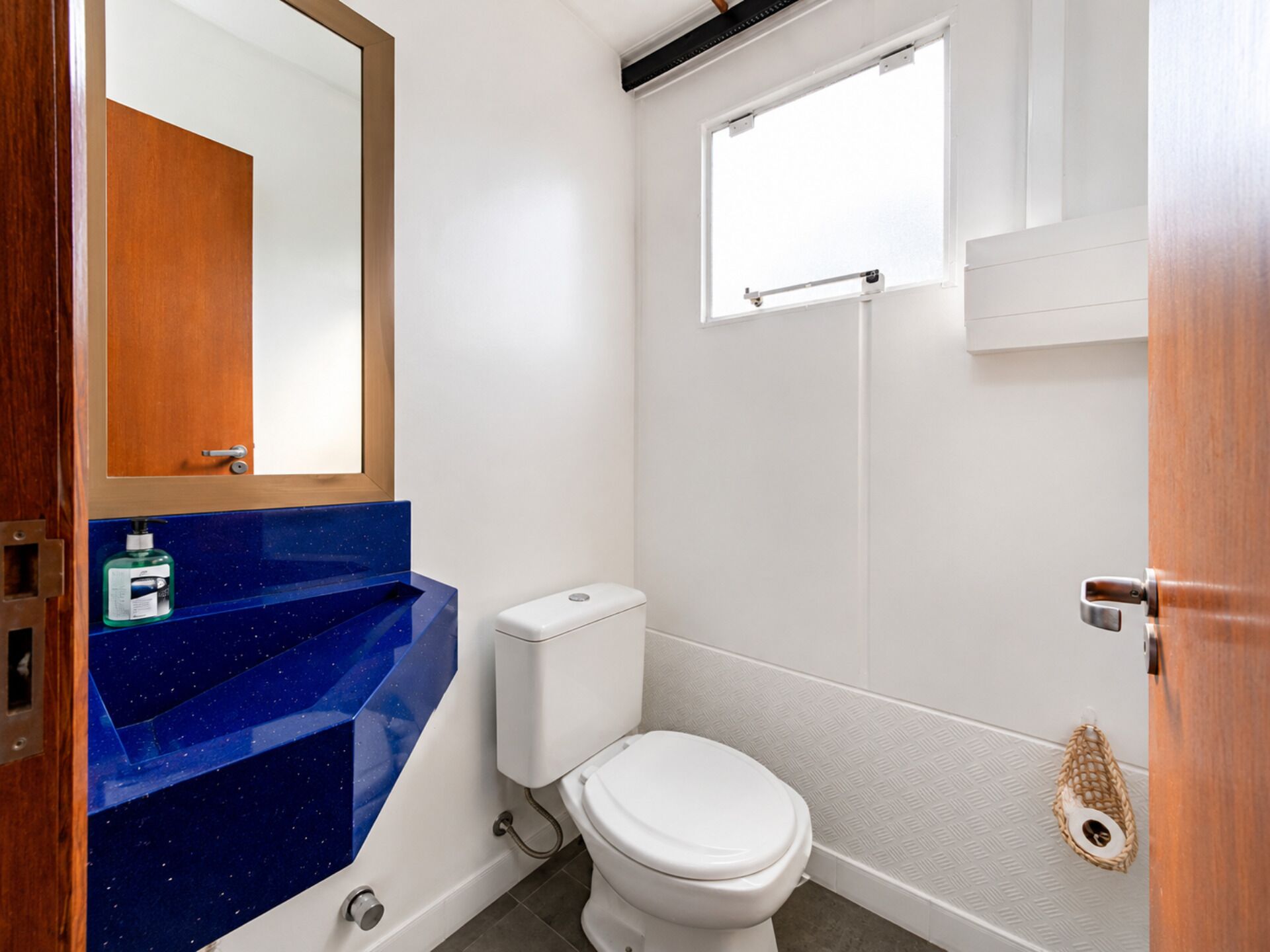 Un baño con inodoro blanco, encimera azul y puerta de madera.