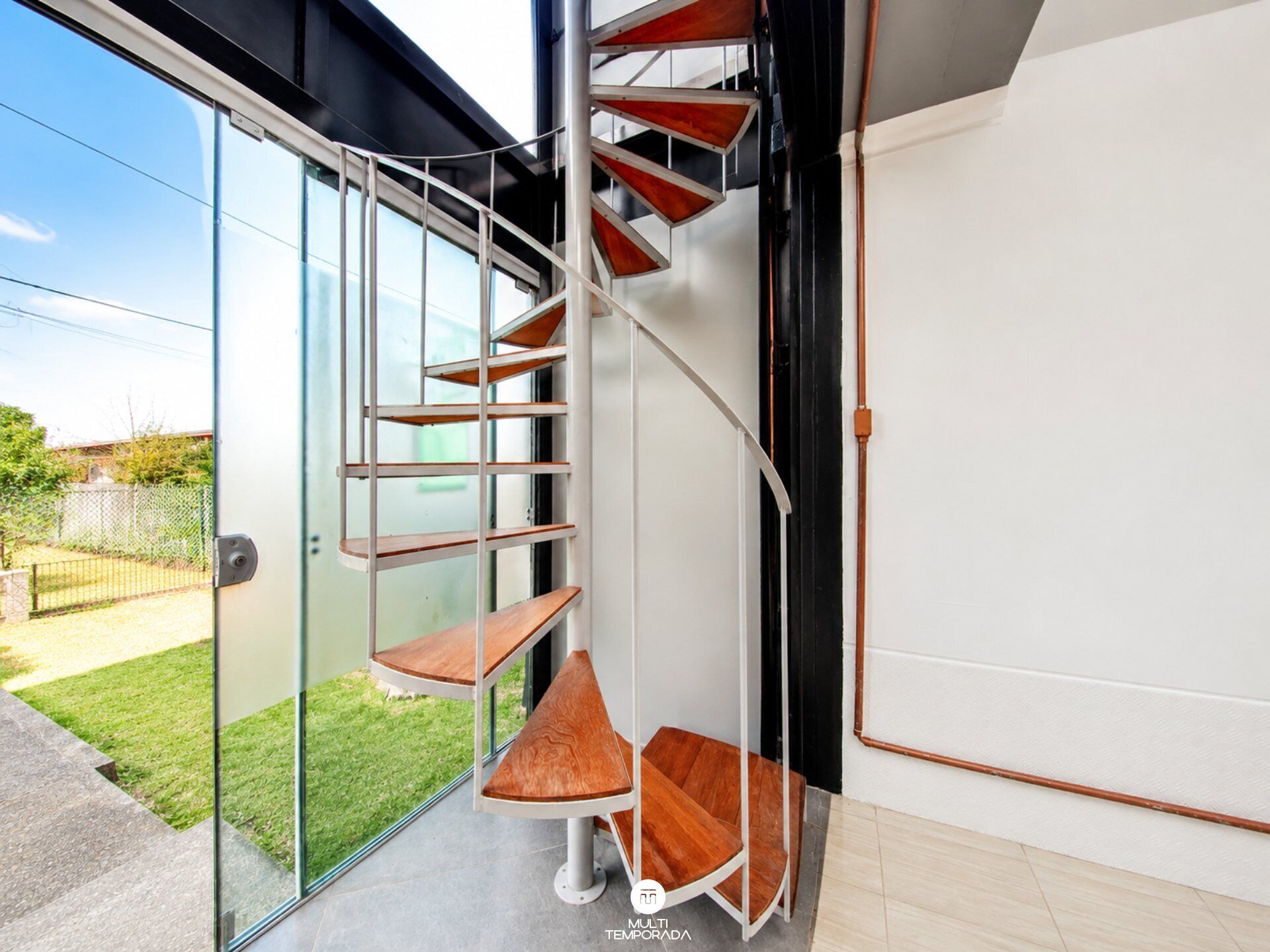 A modern interior with a spiral staircase, a glass door leading outside, and a white wall.