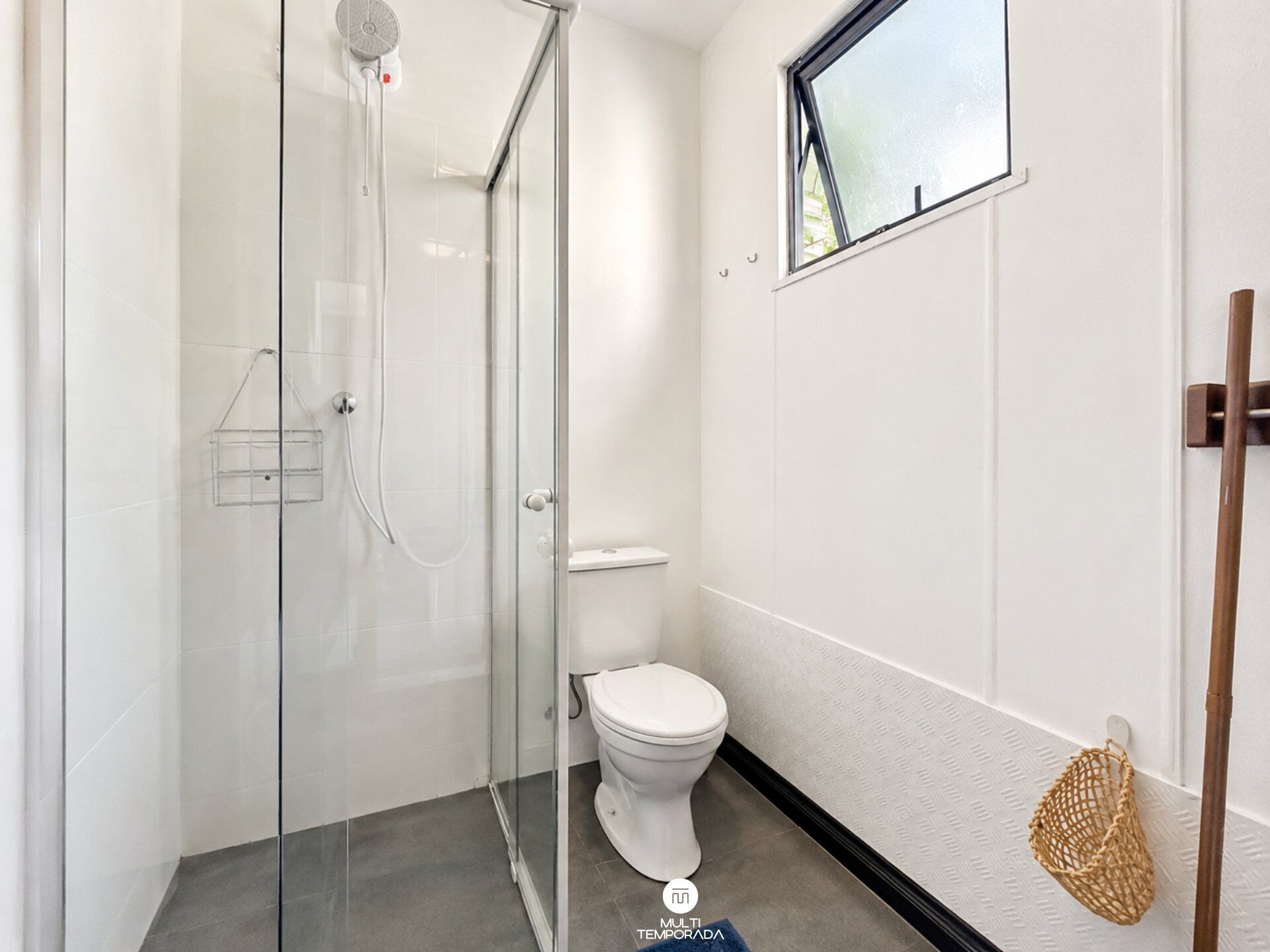A modern bathroom with a glass shower enclosure, a toilet, and a small window.
