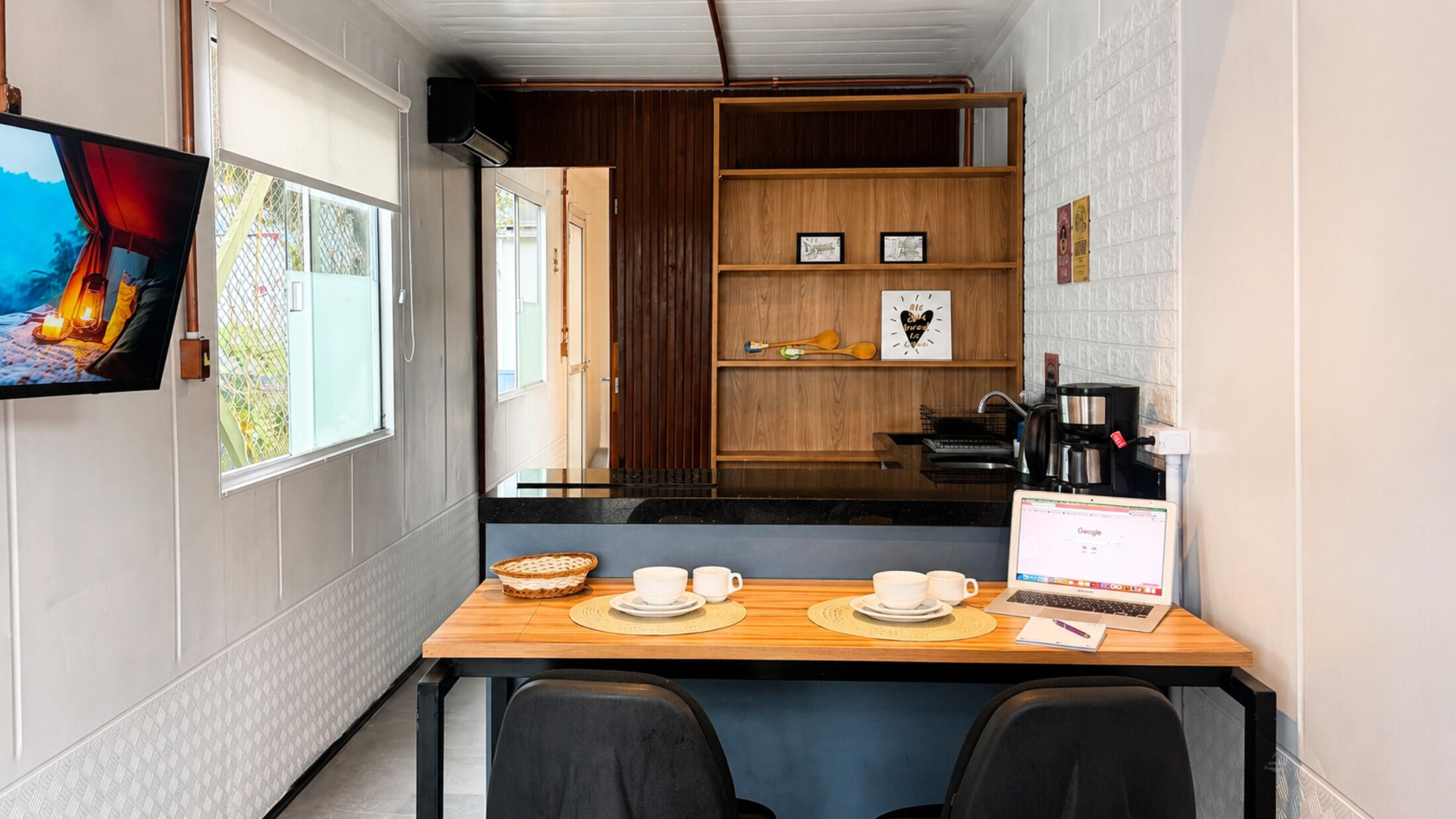 A compact kitchen with a dining table, chairs, a laptop, and a coffee maker.