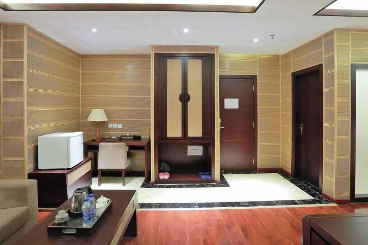 A hotel room with a wooden panel wall, a desk with a lamp, a small refrigerator, a coffee maker, and a tray with bottles and glasses.