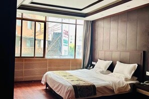 A hotel room with a large window, a bed with white linens, and a wooden headboard.