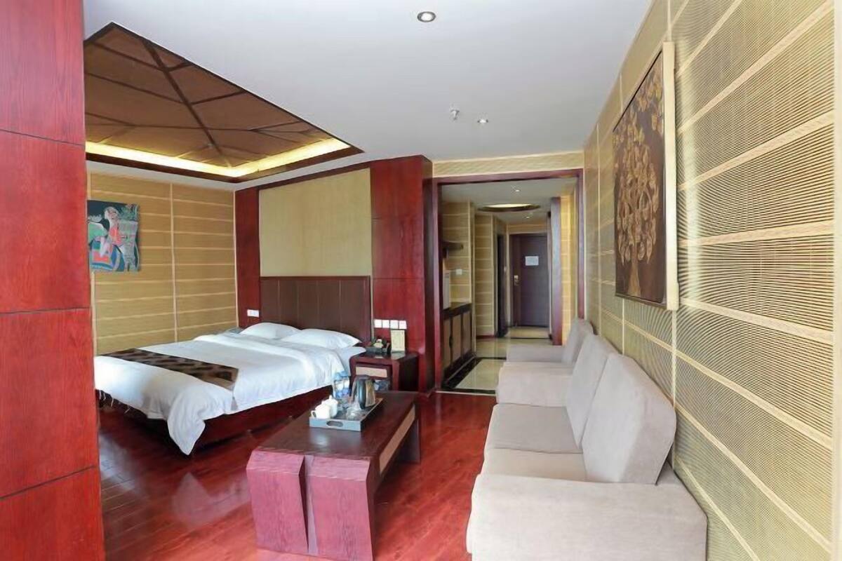 A hotel room with a bed, a sofa, a coffee table, and a painting on the wall.