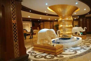 A lobby with a large golden fountain, white elephant sculptures, and a patterned floor. - Mengla Zai Ya Ge Ha Hotel (Mengla)