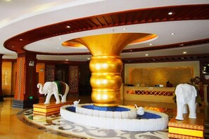 Eine Lobby mit einer großen, goldenen Säule, einem Empfangsschalter und dekorativen Elefantenstatuen.