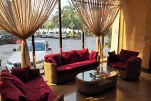 A seating area with a sofa and chairs, a glass-top coffee table, and a view of the parking lot through large windows. - Mengla Zai Ya Ge Ha Hotel (Mengla)