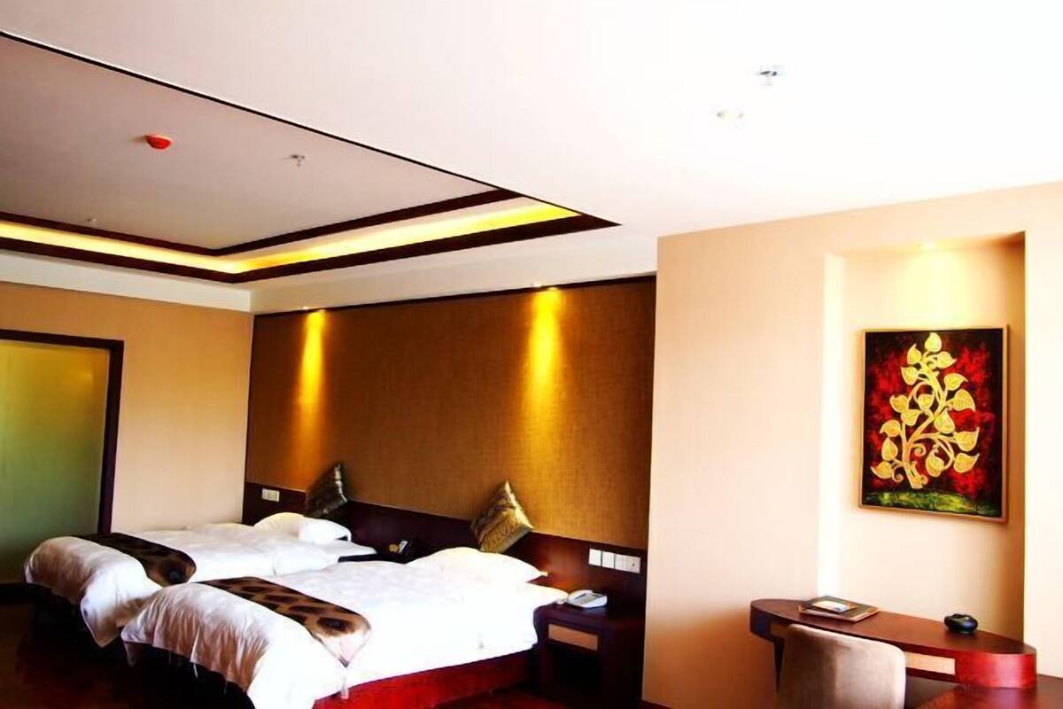 A hotel room with two beds, a desk, and a painting on the wall.