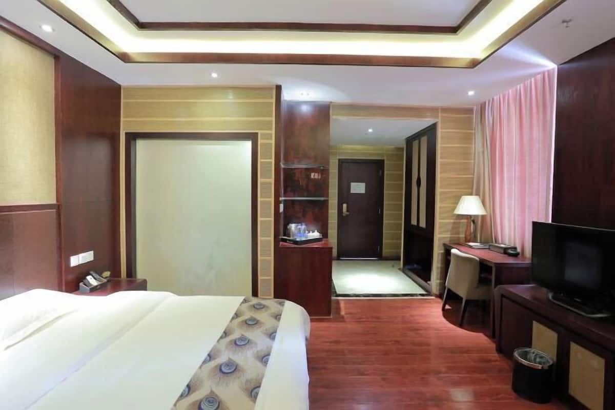 A hotel room with a bed, desk, television, and a small seating area.