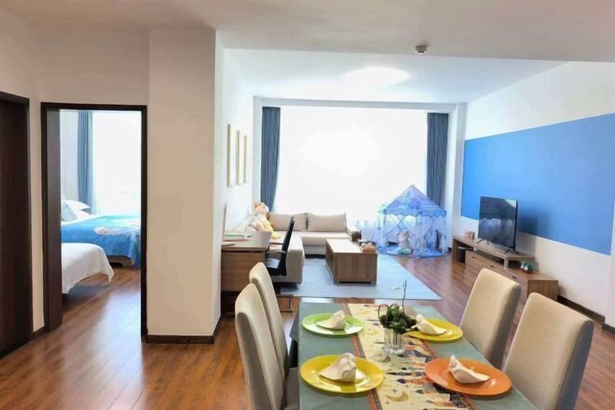 Quarto de hotel moderno com área de refeições, sofá, TV e varanda.