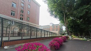 A covered walkway with glass panels, surrounded by brick buildings and trees. - Changchun Nanhu Hotel Qingyue Villa Holiday Apartment (Changchun)