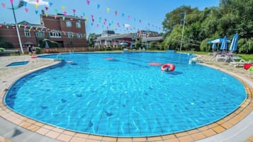 A large circular swimming pool with a tiled edge, surrounded by lounge chairs and umbrellas.