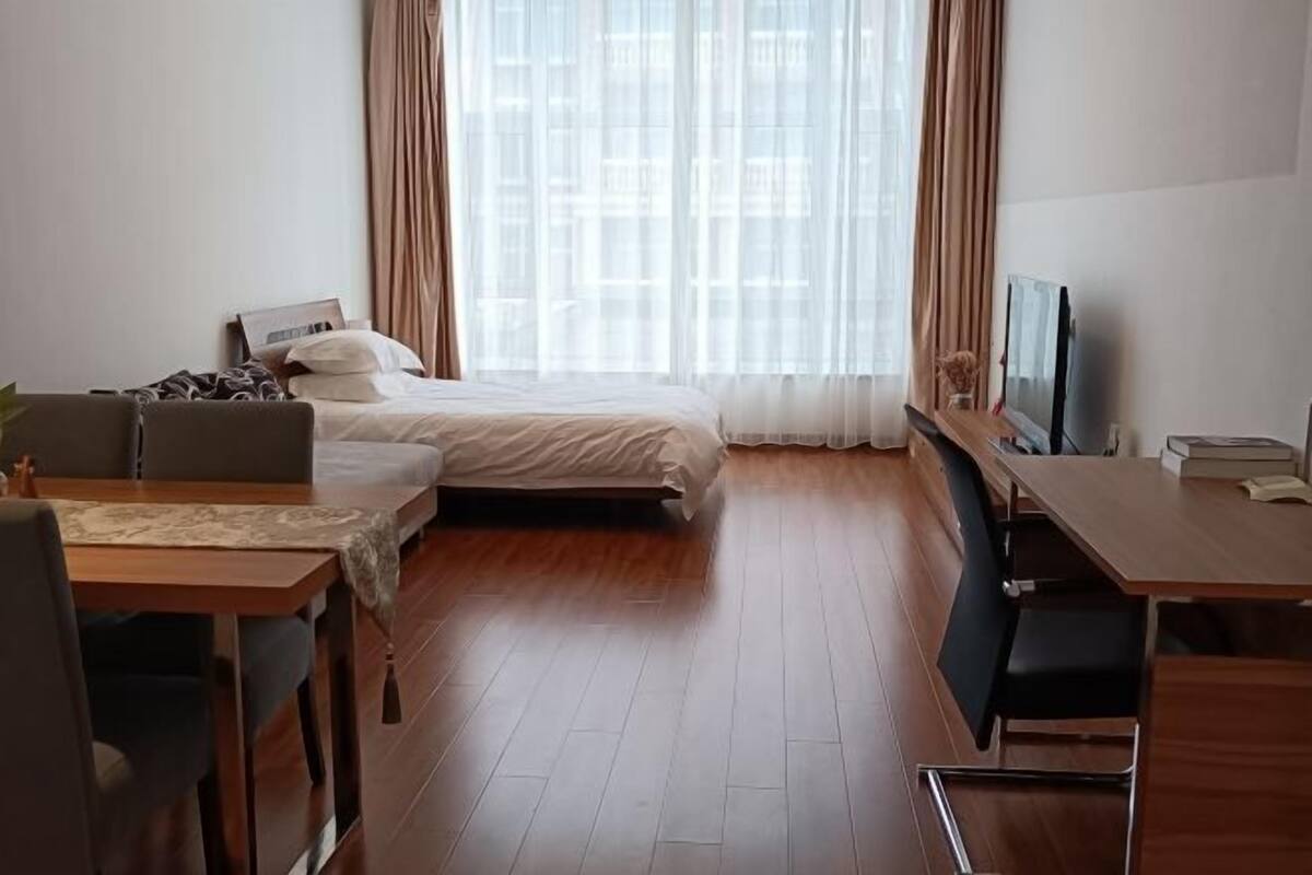 Quarto de hotel com cama, escrivaninha, cadeira, televisão e janela com cortinas.