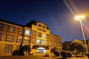 A multi-story building with a prominent entrance, likely a hotel or similar establishment, featuring a covered walkway and well-maintained landscaping.