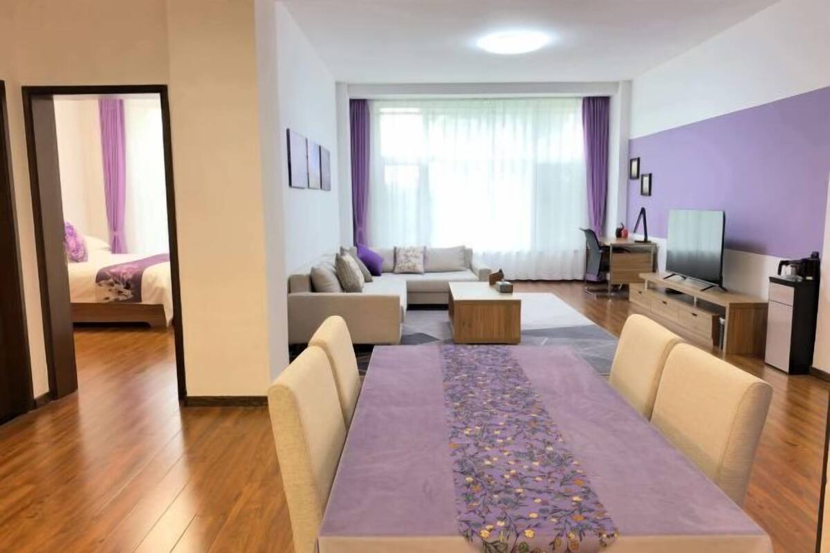 Uma sala de estar moderna com uma mesa de jantar, sofás, uma TV e uma área de cozinha.