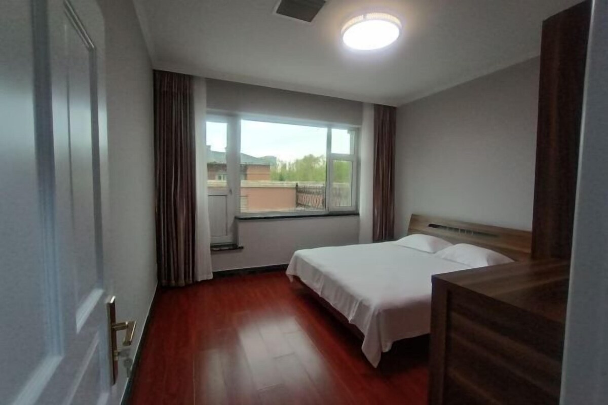 Une chambre d’hôtel avec un plancher en bois, un lit avec du linge de maison blanc, une fenêtre avec des rideaux et une vue sur l’extérieur.