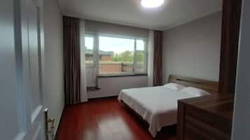 A hotel room with a wooden floor, a bed with white linens, a window with curtains, and a view of the outside.