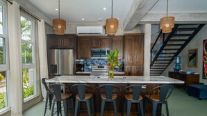 A modern kitchen with dark wood cabinets, a stainless steel refrigerator, and a large island with bar stools. - Conmigos 6 Bedroom Beachfront Villa (Placencia)