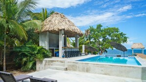 A pool area with lounge chairs, a bar, and a thatched-roof structure. - Conmigos 6 Bedroom Beachfront Villa (Placencia)