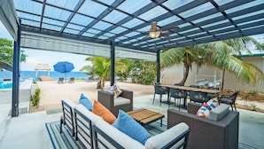 A covered outdoor seating area with a pool, lounge chairs, and a table. - Conmigos 6 Bedroom Beachfront Villa (Placencia)