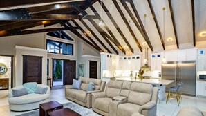 Amplia sala de estar con techo alto y vigas a la vista, cocina equipada con electrodomésticos modernos y un acogedor conjunto de asientos.