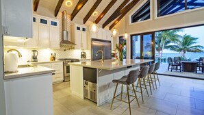 Una cocina moderna con armarios blancos, un refrigerador de acero inoxidable y una barra con taburetes.