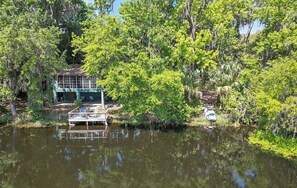 A house by a lake surrounded by dense trees. - Rustic Lakehouse kayaks fishing bonfires (Inverness)