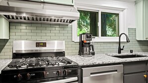 Een keuken met een gasfornuis, koffiezetapparaat en een raam met uitzicht op bomen.