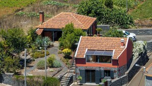 Uma casa de dois andares com telhado de telhas vermelhas, fachada de pedra e painel solar no telhado.