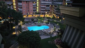 A rooftop pool area with lounge chairs and umbrellas, surrounded by greenery and adjacent to a multi-story building with balconies. - Rome Phoenix Suite cozy elegant, terrace and pool dream eur center (Roma)