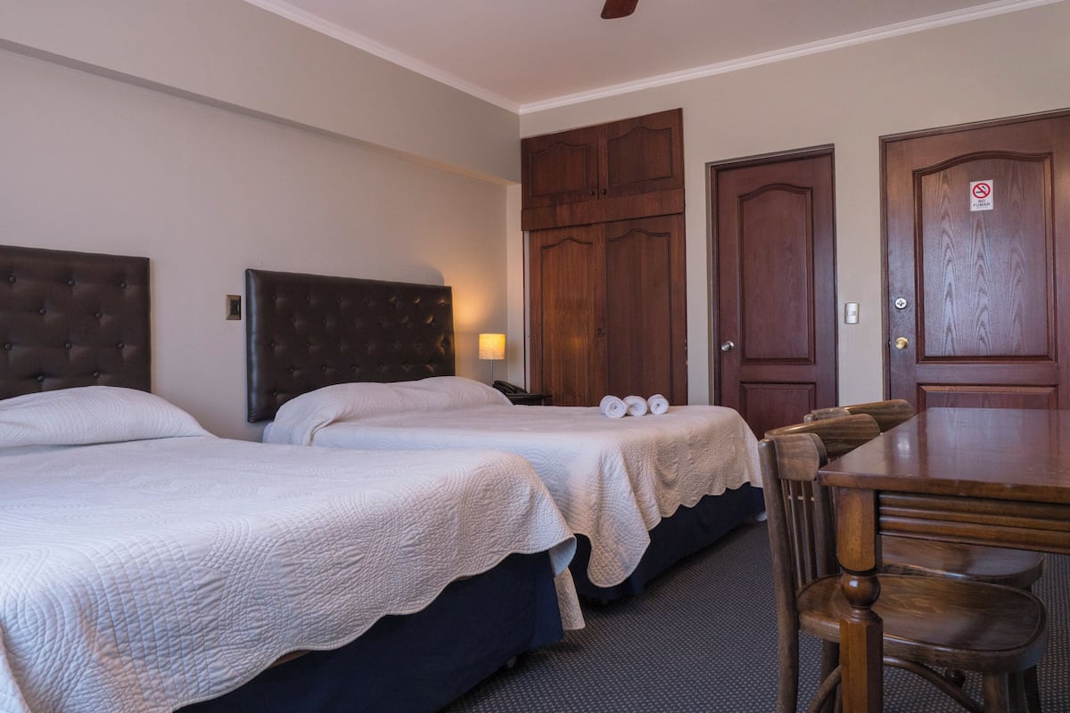 A hotel room with two beds, a wooden table, and a ceiling fan.