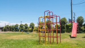 A playground with various play structures, including a climbing frame and slides, set in a grassy area with trees and a clear sky in the background. - Econohotel (Los Angeles)