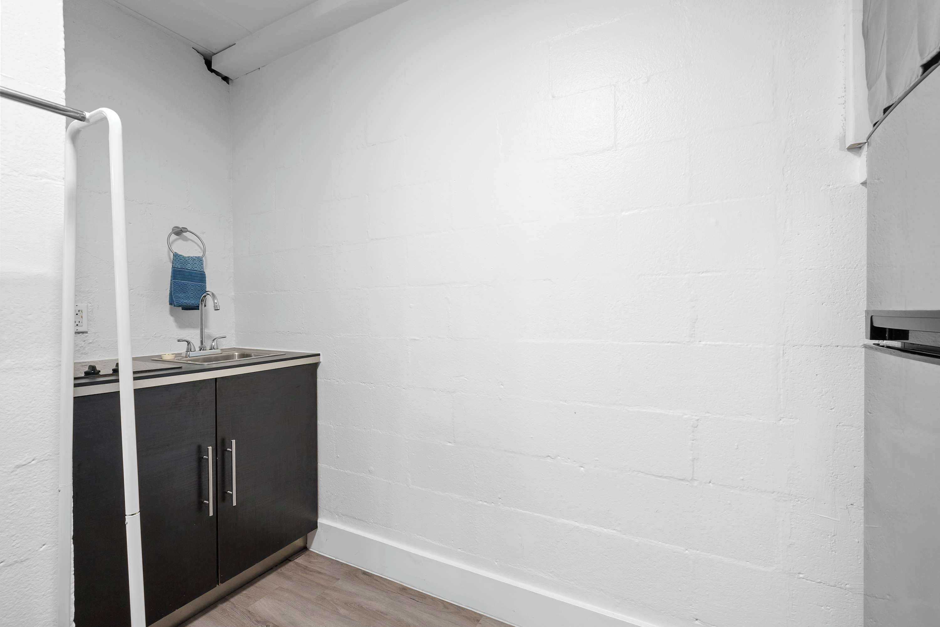 A small, compact bathroom with a white brick wall, a dark-colored cabinet with a sink, and a towel rack.