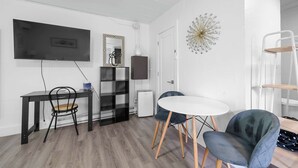 Una sala de estar moderna con un televisor de pantalla plana, una mesa redonda blanca, dos sillones, una estantería y un adorno en la pared.
