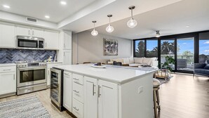 Une cuisine moderne avec des meubles blancs, un grand îlot central, des appareils en acier inoxydable et des luminaires suspendus.