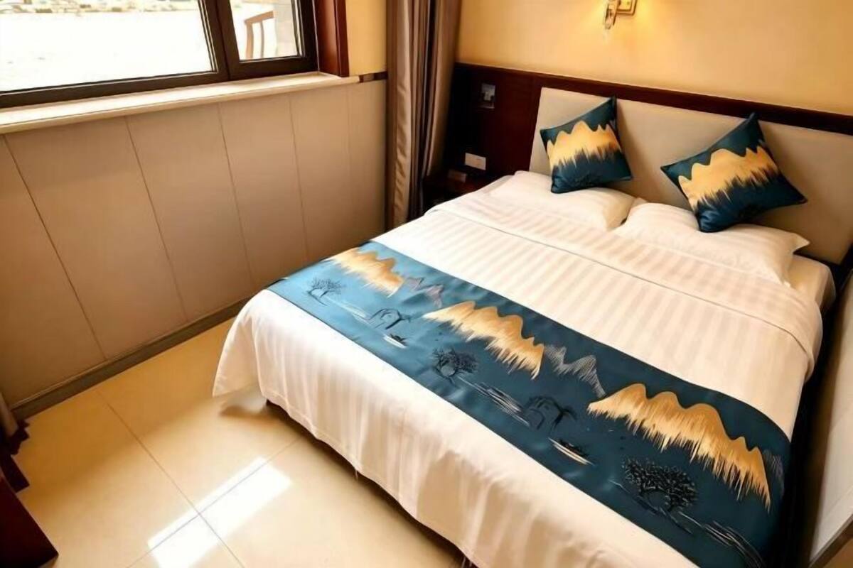 A hotel room with a bed, a nightstand, a window, and a wall-mounted light fixture.