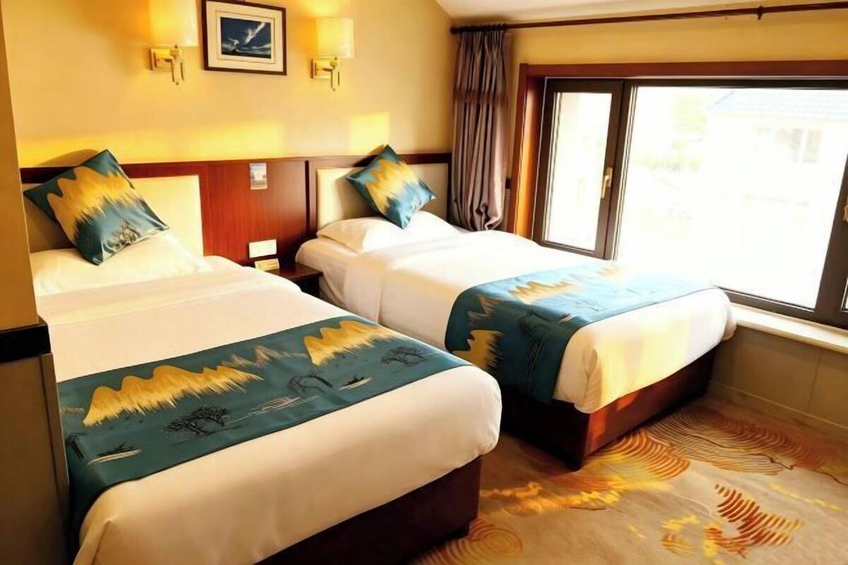 A hotel room with two beds, a window with curtains, and a wall-mounted light fixture.