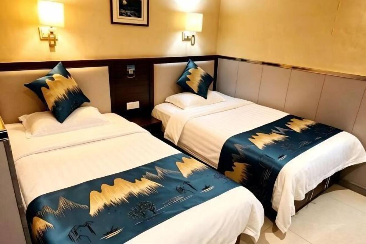 A hotel room with two single beds, each with a headboard, bedside tables, and lamps.