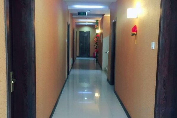Pasillo de hotel con puertas a ambos lados, un adorno iluminado en la pared y un suelo reflectante.