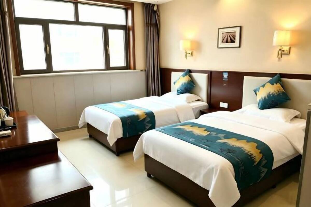 A hotel room with two beds, a desk, and a window with curtains.