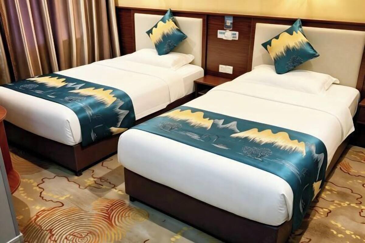 Two adjacent beds with matching headboards and decorative pillows, a patterned carpet, and a wooden nightstand with a lamp.