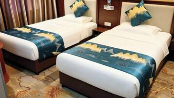 Two adjacent beds with matching headboards and decorative pillows, a patterned carpet, and a wooden nightstand with a lamp.