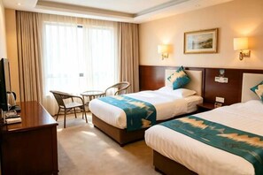 Habitación de hotel con dos camas, un escritorio, una silla y una ventana con cortinas.