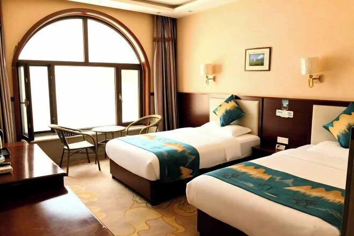 A hotel room with two beds, a desk, a chair, and a large arched window.