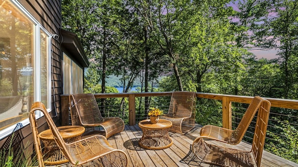 Una terraza de madera con sillas de mimbre y una pequeña mesa, con vistas a un área boscosa.