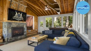 Una sala de estar acogedora con chimenea de piedra, un televisor grande montado en la pared y un cómodo sofá azul.