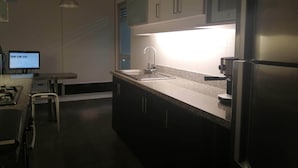 A modern kitchen with a stainless steel refrigerator, a sink, and a countertop. There is a dining area with a table and chairs, and a computer monitor on the wall. - Cozy apartment in Lima, in a club house. (Santiago de Surco)
