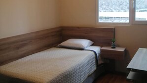 A small, cozy room with a wooden bed, a bedside table with a lamp, and a window with a view of a snowy landscape. - Cozy apartment in Lima, in a club house. (Santiago de Surco)