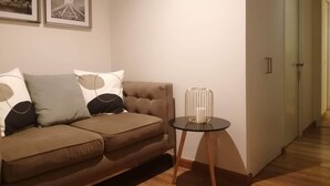 A living room with a brown sofa, two framed pictures on the wall, and a small table with a glass vase. - Cozy apartment in Lima, in a club house. (Santiago de Surco)