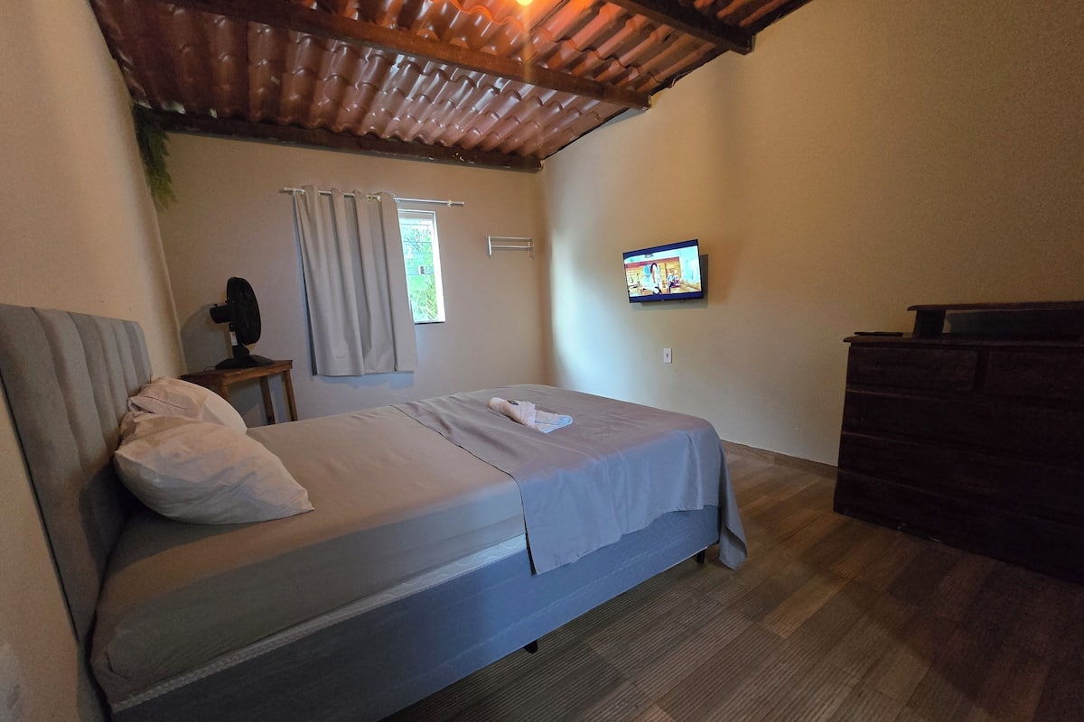 Una camera da letto con un letto, una televisione, una cassettiera e una finestra con tende.